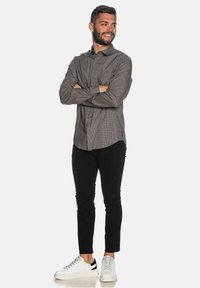 Camicia a quadri grigia con bottoni, pantaloni neri slim e sneakers bianche con accenti neri. La camicia ha un colletto classico e maniche lunghe.
