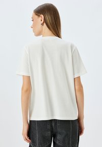 Valkoinen puuvillapaita, jossa on rento leikkaus, lyhyet hihat ja suora helma. Takana on sileä pinta ilman näkyviä printtejä tai yksityiskohtia.