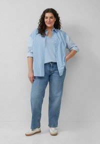  Lichtblauw gestreept overhemd met knopen over een effen lichtblauw top, gecombineerd met losse denim jeans en beige sneakers met witte accenten.