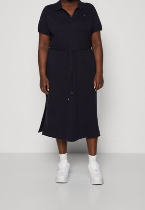 Marineblauwe jurk met korte mouwen, een kraag, een getailleerde taille, zijslits en een gladde textuur, gecombineerd met witte sneakers.