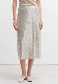 Silberner Midrock aus vertikalen Pailletten, mit glatter Textur und einem taillierten Bund. Kombiniert mit hellrosanen flachen Schuhen.