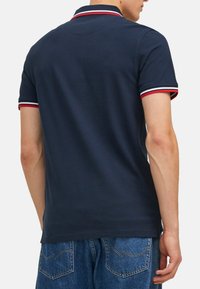Marineblauw poloshirt met rood-witte gestreepte kraag en mouwbanden, gemaakt van gladde stof, heeft een klassieke pasvorm en korte mouwen.