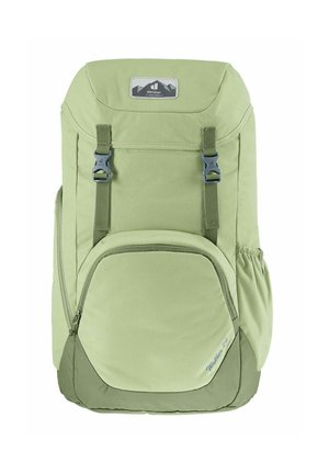 Mochila de tela verde con correas ajustables, un bolsillo frontal con cremallera, un bolsillo lateral elástico y un diseño redondeado. Presenta una etiqueta de logo en la parte superior.