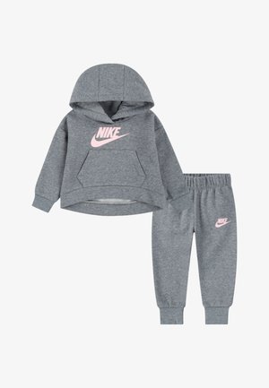 Sivi pamučni dukserica s ružičastim Nike logotipom sprijeda, uparen s odgovarajućim sivim trenirkama koje imaju mali ružičasti Nike logotip.