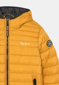 Chaqueta acolchada amarilla con capucha, cremallera negra, logo de Pepe Jeans en el pecho y parche en la manga que dice "London 1973 Pepe Jeans".