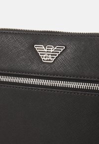 Pouch in pelle nera con texture, zip argentata e logo ad aquila Armani argentato al centro in alto.