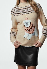 Pull en maille beige doux avec un graphique d'ours polaire, yoke à motifs en marron et bleu, finitions côtelées aux poignets et à l'ourlet, associé à une jupe en cuir noire.