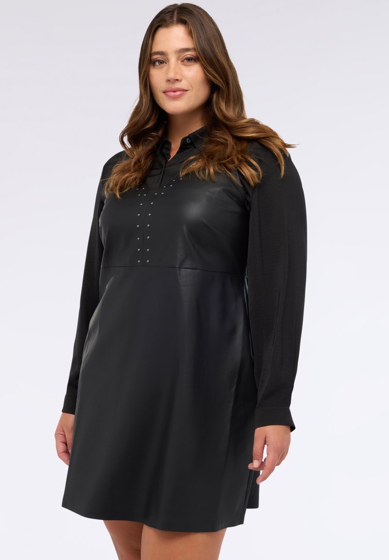 Schwarzes Kleid mit einem gerafften Leder-Oberteil, langen Ärmeln aus einem weichen Stoff und silbernen Nieten entlang der Vorderseite für zusätzliche Akzente.
