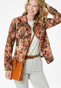 Denimjack met bloemenpatroon in warme tinten, met lange mouwen, twee borstzakken en een kraag; gecombineerd met een beige leren schoudertas.