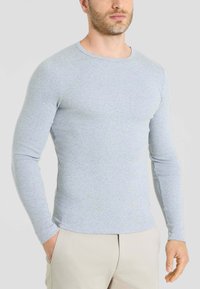 T-shirt a maniche lunghe grigio chiaro realizzato in tessuto morbido, con scollatura a girocollo e design aderente, abbinato a pantaloni beige.