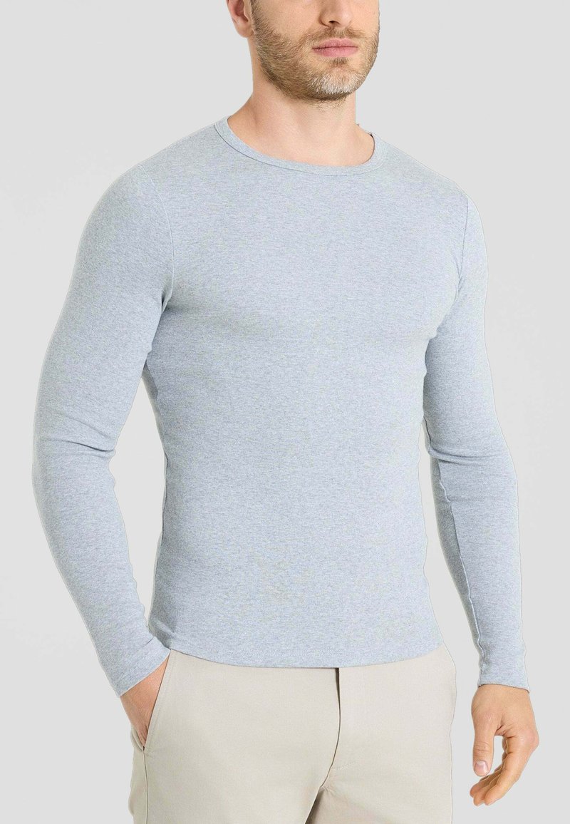 T-shirt a maniche lunghe grigio chiaro realizzato in tessuto morbido, con scollatura a girocollo e design aderente, abbinato a pantaloni beige.