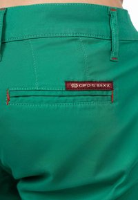 Pantaloni verdi con una tasca posteriore caratterizzata da cuciture rosse e un'etichetta bordeaux con la scritta 'Cipo & Baxx'.