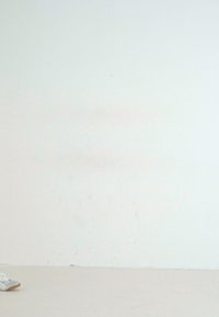 Gray athletic shoes with a textured upper, laces, and a brown rubber sole, positioned against a plain white wall.