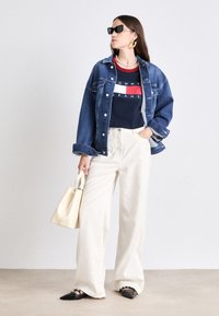 Denimjakke, marineblå Tommy Jeans t-shirt med rød og hvid stribe, cremede vidde bukser, sorte spidse sko og en beige tote bag.