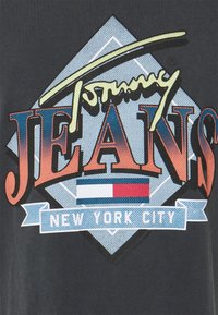 Svart t-shirt med en färgglad grafikdesign där det står "Tommy JEANS" i röd och blå, och "NEW YORK CITY" på ett band längst ner.