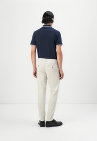 Marineblauw poloshirt met witte afwerking, gecombineerd met crèmekleurige broek. Gladde stof met een getailleerde pasvorm en twee achterzakken. Zwarte schoenen.