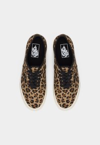 Ζεύγος καφέ και μαύρων αθλητικών Vans με σχέδιο λεοπάρδαλης, μαύρα κορδόνια και λευκές σόλες, καθώς φαίνονται από πάνω σε λευκό φόντο.
