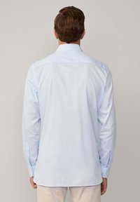 Camicia azzurro chiaro a maniche lunghe con colletto classico, polsini abbottonati e una texture liscia. Design semplice, il tessuto scivola dolcemente.