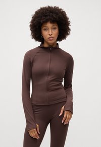 Smeđa zip-up jakna za aktivne sportove s dugim rukavima, napravljena od glatkog, rastezljivog materijala. Ima raglan rukave i visoki ovratnik.