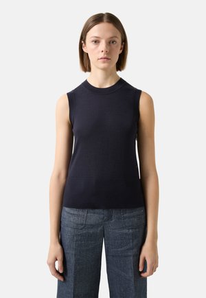 Navy sleeveless knit top with a round neck, featuring a ribbed texture and subtle seam detail at the hem; paired with denim trousers.