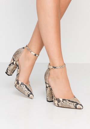 Zapatos de tacón alto tipo pump en estampado de serpiente beige y negro, con punta puntiaguda y pulsera en el tobillo, con un acabado texturizado similar al cuero.