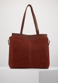 Sac fourre-tout en daim marron avec un dessus en cuir lisse, deux poignées et une fermeture zippée. Présente un design simple sans motifs visibles.