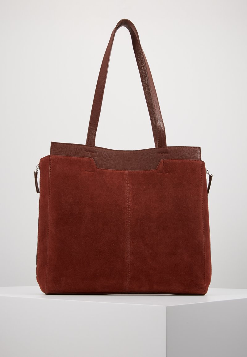 Sac fourre-tout en daim marron avec un dessus en cuir lisse, deux poignées et une fermeture zippée. Présente un design simple sans motifs visibles.