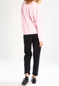 Lasroze trui met een relaxte pasvorm en ribgebreide manchetten, gecombineerd met zwarte opgerolde jeans en glanzende zwarte schoenen.