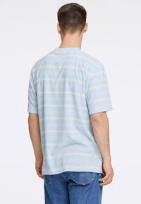 Ljusblå kort ärmad skjorta med horisontella beige ränder, mjukt material, rund hals och avslappnad passform. Bärs med blå jeans.