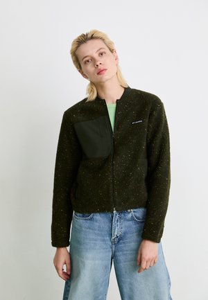 Fleecejakke i mørkegrønn med glidelås foran, med en teksturert overflate, en solid lomme og rund hals. Brukt med lyseblå jeans.