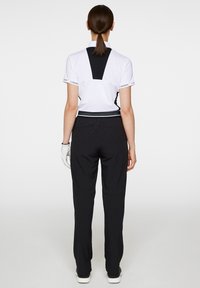 Vit kortärmad polo med svart bakpanel, matchad med svarta byxor. Ensemblen har en texturerad midjeband och subtila logotypdetaljer.