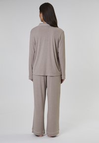 Lichtbruin loungewear set gemaakt van zachte stof. Het lange mouwen bovenstuk heeft een kraag; de brede broekspijpen hebben een witte rand aan de onderkant.