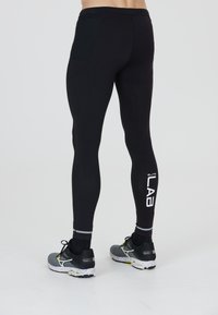 Zwarte sportleggings met een slim fit, netstof pocketdetails en een bedrukte "ELITE LAB" logo. Gecombineerd met grijze hardloopschoenen met een gespikkelde zool.