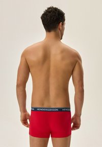 Czerwone bokserki wykonane z miękkiego materiału, z szerokim granatowym pasem w białe litery. Widok pokazuje tył odzieży.