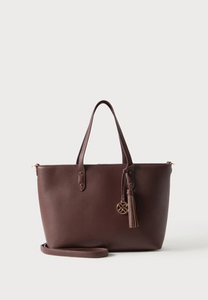 Borsa tote in pelle marrone con doppio manico, tracolla removibile e nappina decorativa con emblema dorato.