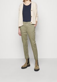 Beige cardigan med guldknappar, marinblå topp, olivgröna byxor och bruna ankelstövlar med svarta detaljer och texturerad sula.