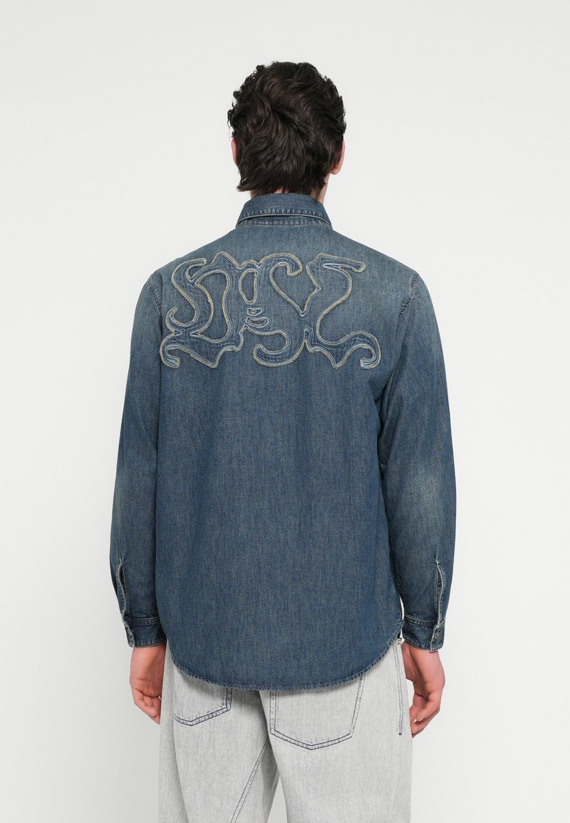 Πουκάμισο από τζιν σε σκούρο μπλε με μακριά μανίκια, με μεγάλο κεντητό σχέδιο στην πλάτη. Απαλή υφή, ίσια ραφή στο τελείωμα, μανσέτες με κουμπιά.