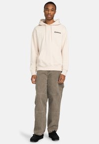 Sweat-shirt à capuche beige clair avec le logo "Element", associé à un pantalon cargo vert olive ample et des chaussures noires.