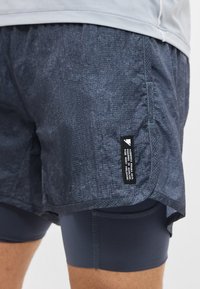 Κοντινή λήψη σκούρων μπλε αθλητικών σορτς με ενσωματωμένα ελαστικά κολάν και μια μαύρη ετικέτα στην εξωτερική πλευρά κοντά στο τελείωμα.