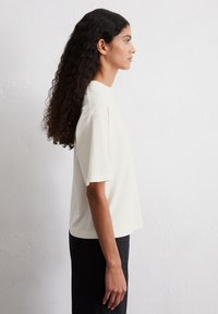 T-shirt crema a maniche corte con una vestibilità rilassata e scollatura rotonda. Texture liscia, design minimalista, abbinato a un pantalone nero.
