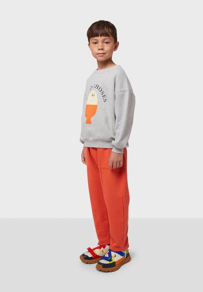 Sudadera gris con un gráfico naranja, combinada con pantalones anaranjados holgados. El calzado presenta detalles multicolores con suelas texturizadas.
