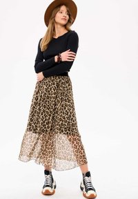 Leoprint chiffon rok met een zwart aansluitend T-shirt met lange mouwen, gecombineerd met chunky zwart-witte sneakers en een bruine brede hoed.