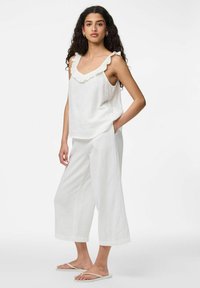 Ensemble blanc léger en deux pièces avec un haut sans manches à col volanté et un pantalon à jambes larges, tous deux en tissu texturé.