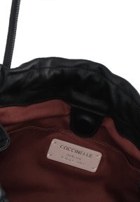 Borsa in pelle nera con una parte superiore morbida e arricciata, dotata di una fodera in tessuto bordeaux e un'etichetta crema con la scritta "Coccinelle Authentic Italian Leather."