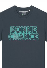Donkerblauwe katoenen T-shirt met "BONNE CHANCE" in grote, vetgedrukte turkooise letters. Ronde halslijn met korte mouwen, casual fit.