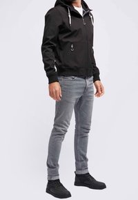 Svart zip-up hoodie med dragsnören, dubbla sidofickor och ribbade muddar, i kombination med ljusgrå jeans och svarta sneakers.