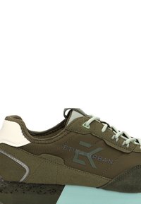 Zapatillas verde oliva con parte superior de ante, acentos crema, suela negra texturizada y detalles verde claro. Cuenta con cierre de cordones y marca.