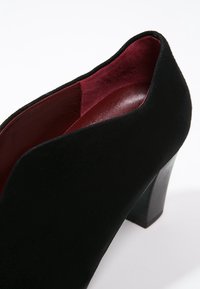 Chaussure à talon haut en daim noir avec un bout arrondi et un intérieur bordeaux, dotée d'un talon carré épais et d'une texture lisse.