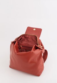 Bolso de cuero rojo con un diseño suave y flexible. Acentos de hardware dorado, cierre de cremallera, forro de tela y bolsillos interiores para organización.