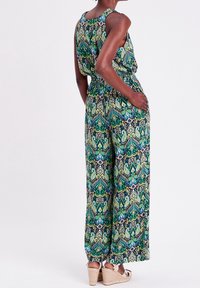 Combinaison sans manches en imprimé paisley vert et bleu. Dotée d'une taille cintrée et de jambes larges, fabriquée en tissu léger.